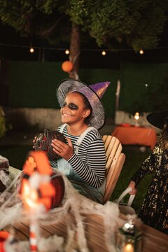 Girl in witch hat and face paint enjoying Halloween celebrations at night
