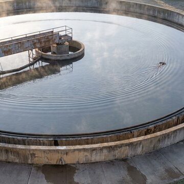 Still water and steam rising over a circular clarifier tank at dawn