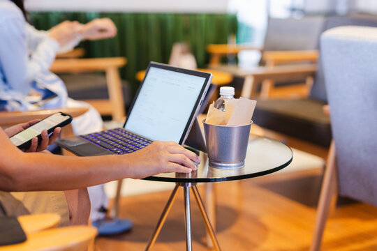 Business woman holding a smartphone while using a laptop in co working lounge.
