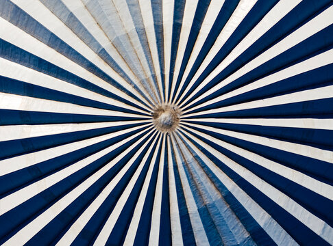 ymmetrical low-angle abstract view looking up at a circular dome ceiling with a radiating sunburst pattern of dark blue and white stripes. Modern graphic architectural background.