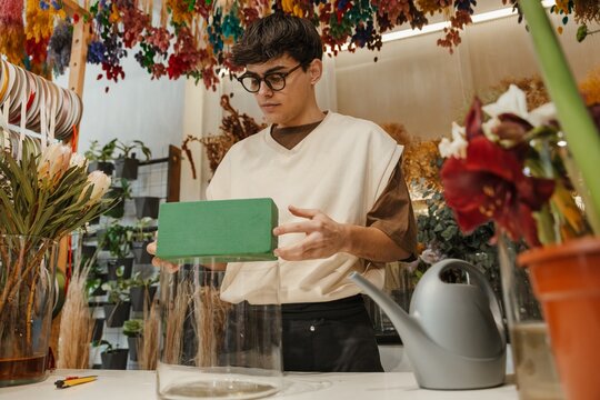 Young male florist holding floral foam in a colorful flower shop