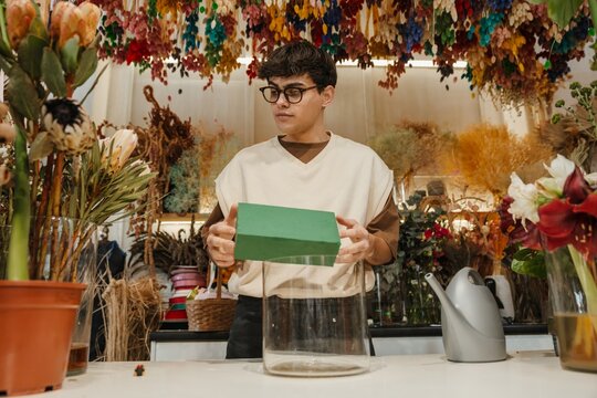 Young male florist placing floral foam in a container in a colorful flower shop