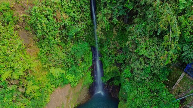 Aerial view of Curug Telu waterfall cascading into a lush green jungle pool in Baturaden, Jawa Tengah, Indonesia.