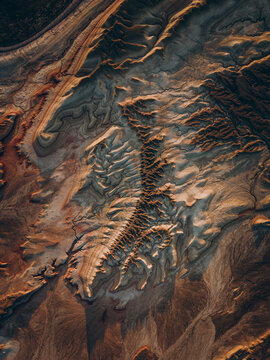 Layered ridges and winding channels form a dramatic geological landscape in brown and charcoal tones, creating an artistic natural texture shaped by erosion and time.