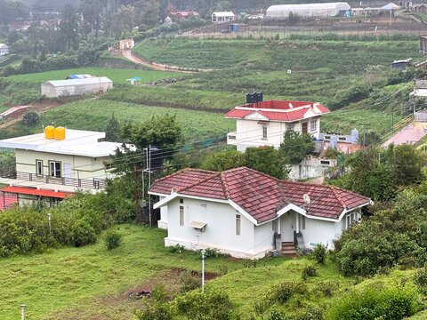 Misty hill station resort with red tiled cottages surrounded by lush green tea plantations, eucalyptus trees and foggy mountain slopes, capturing peaceful monsoon travel and countryside retreat.