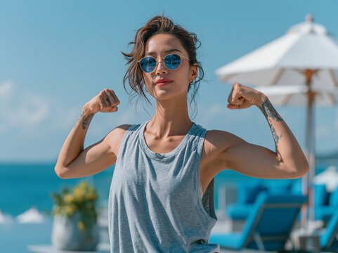Healthy woman wearing blue tank top and sunglass show her arm muscle , sea view is background , holiday mood.