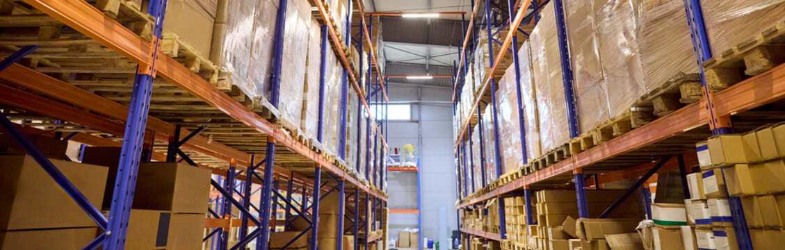 Warehouse shelves with pallets, boxes and inventory. Tall storage racks form a bright aisle for logistics, distribution and stock control. Concept shows efficient organized warehouse storage.