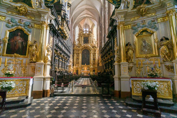 Fototapeta premium The magnificent high altar and dark wood choir stalls inside the 14th-century Corpus Christi Basilica in Kazimierz district of Kraków, Poland. A massive, highly ornate gold Baroque structure. 