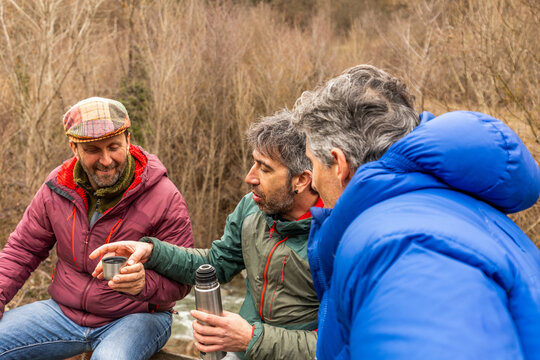 Friends share hot drink beside water in nature