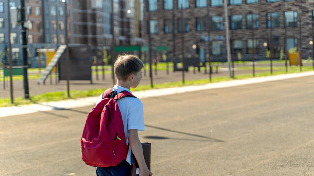 Boy walks toward school, red backpack on shoulder