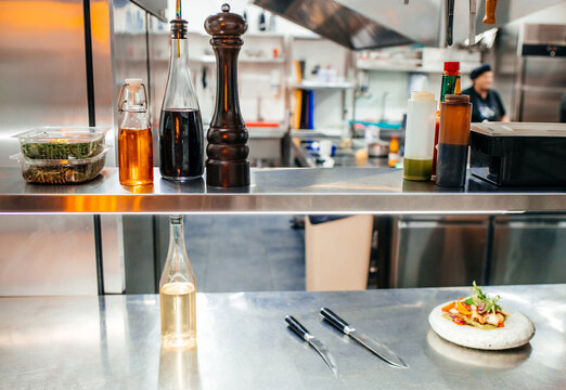 Kitchen countertop with glass bottles of oil and vinegar, pepper mill, and knives, featuring a plate of food in a modern restaurant kitchen setting