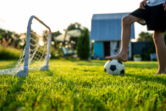 Child kicks ball near small goalpost on grassy field