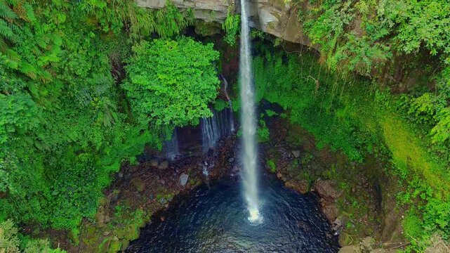 Aerial view of Curug Telu waterfall surrounded by lush green tropical forest in Baturaden, Jawa Tengah, Indonesia.