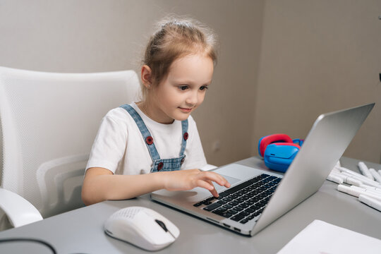 Young girl engaging with laptop, typing on keyboard and using mouse, enjoying online education and digital learning activities from home desk.