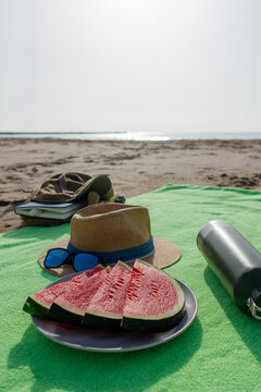 Vertical fresh watermelon with hat and metal water bottle on beach