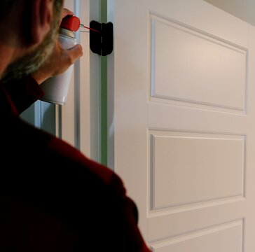 Homeowner applying aerosol silicone lubricant spray grease oil to interior door hinges wiping away residue during routine home maintenance repair work