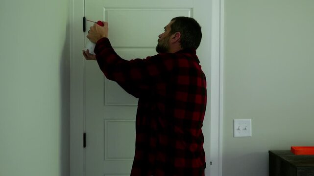 Homeowner applying aerosol silicone lubricant spray grease oil to interior door hinges wiping away residue during routine home maintenance repair work