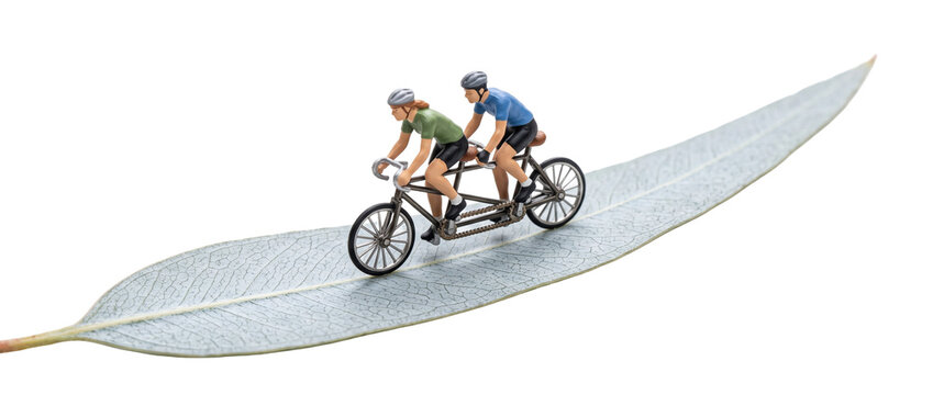 Miniature couple riding tandem bicycle on leaf road for eco transport concept, symbolizing partnership, teamwork, sustainability, green living, togetherness, and outdoor fitness on black background.