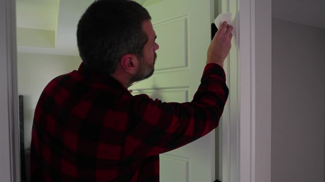 Homeowner applying aerosol silicone lubricant spray grease oil to interior door hinges wiping away residue during routine home maintenance repair work