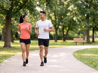 Fototapeta premium Young Southeast Asian couple jogging together in a green park for fitness wellness heart health relationship goals healthy lifestyle and outdoor exercise marketing