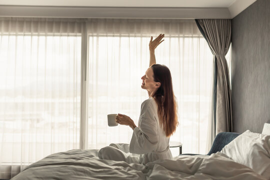 Woman Stretching in Bed With Morning Coffee After Waking Up Feeling Refreshed
