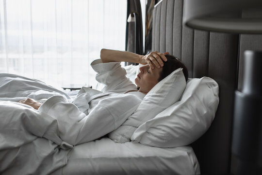 Tired Woman Holding Her Forehead While Lying in Bed in the Morning Feeling Sick
