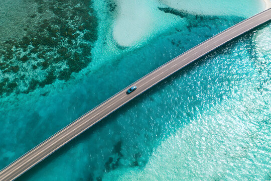 Looking down from above at a vehicle crossing a bridge over the shimmering clear blue ocean in the South Male Atoll, Maldives.