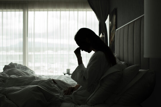 Stressed Woman Sitting in Bed with Head in Hand in the Morning

