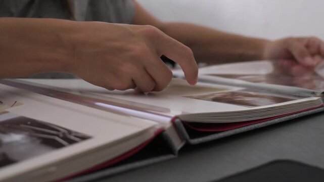 Woman turning pages of open photobook on table while reviewing old memories