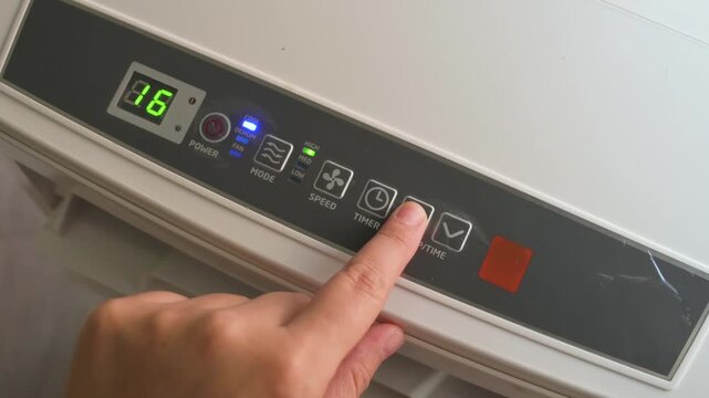 Hand pressing button on digital control panel of portable air conditioner unit