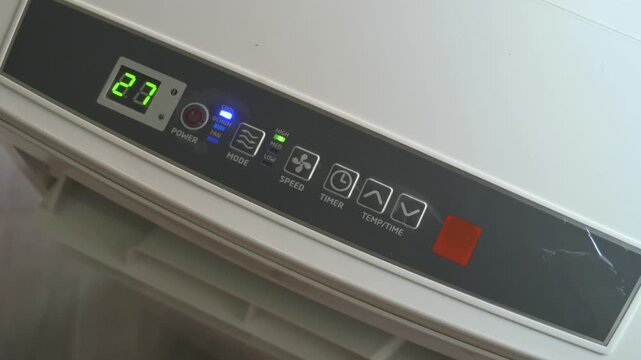 Close up of hand pressing power button to turn on portable air conditioner unit