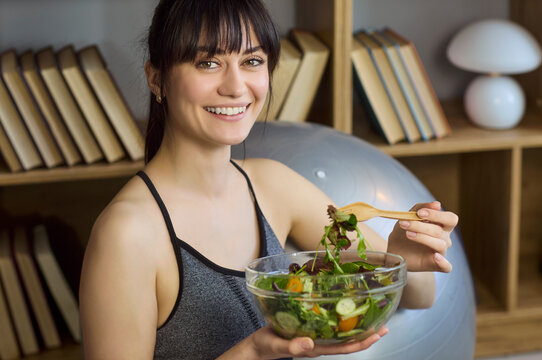 Woman eating salad healthy nutrition fitness lifestyle. She holds a glass bowl of vegetables after workout, promoting balanced meals clean diet and wellness. Concept of healthy living at home.