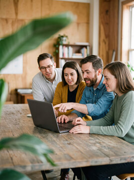 Group of Four People Working Together on a Laptop in a Bright Room