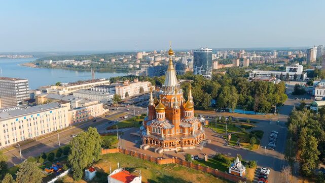 Russia, Izhevsk. Cathedral of the Archangel Michael, red-brick Russian Revival facade with gilded bulbous domes and a soaring 67-metre tent roof, Drone footage over the city and river. Drone footage