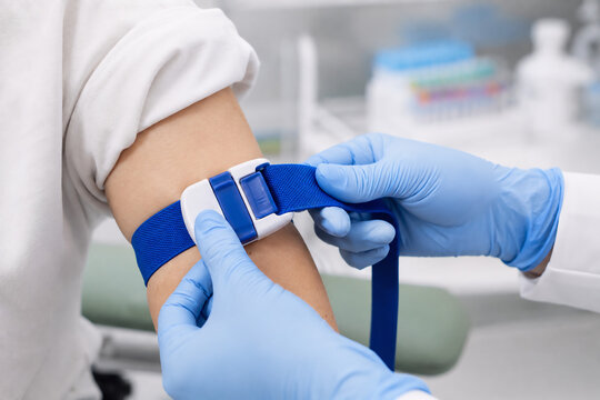 Macro close-up of a nurse's gloved hands tightening a blue quick-release elastic tourniquet around a patient's upper arm before venipuncture, clean bright clinic setting
