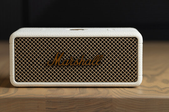 Front view of Marshall Emberton III cream wireless bluetooth speaker with brass grille on wooden table