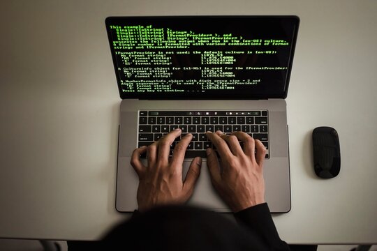 Programmer writing code on laptop with terminal interface screen and computer mouse on white desk, programmer