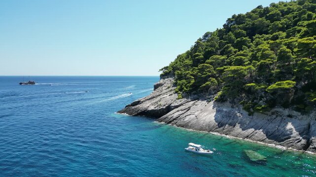 Aerial view of the rocky coastline with lush pine trees and a small boat in the clear blue sea of Zakinthos, Greece.