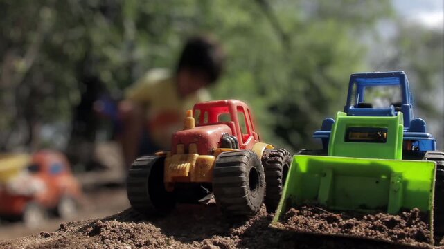 Toy Tractor and Excavator on Soil with Blurred Child in Background - 4K