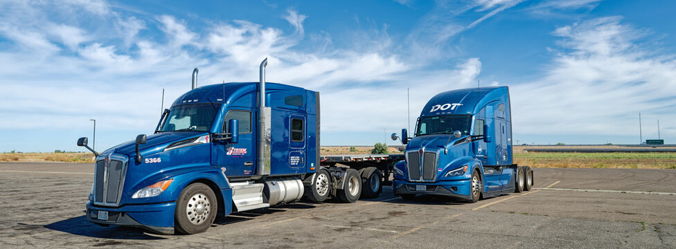 Burley, Idaho, USA - July 3, 2026: Panorama of two blue Kenworth T680 semi trucks from different carriers parked together