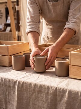 Artisan arranging ceramic candles on linen market table with crates