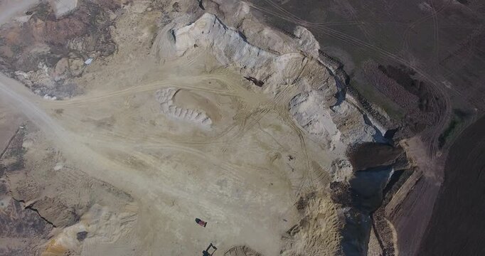 Top down aerial view of a sand quarry with excavators and a truck working the open pit, tire tracks and spoil heaps beside a ploughed field in early spring sunlight