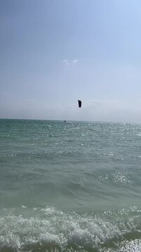 Vertical HD tracking shot of a kitesurfer gliding across the turquoise Indian Ocean in Paje, Zanzibar. The camera follows the black kite flying high under a clear sunny sky.