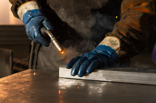 Close up of gloved hands welding metal piece with active torch