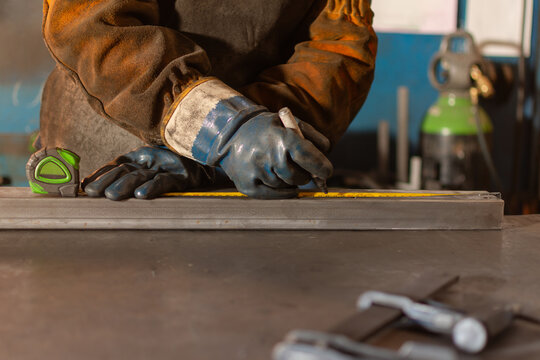 Close up of gloved hands measuring and marking metal for fabrication