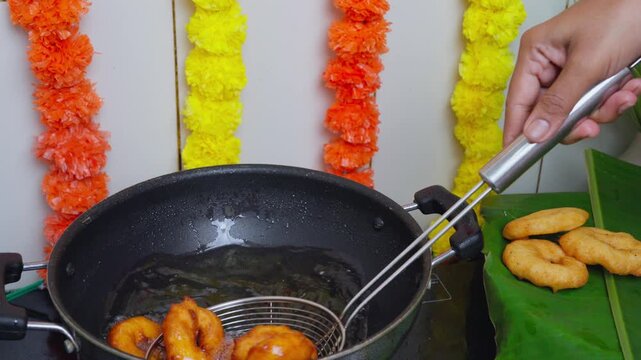 Freshly fried medu vada lifted from hot oil with a slotted spoon