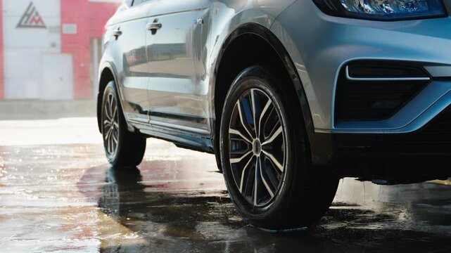 Silver SUV parked wet ground, raindrops gleam. Water drips from tire, reflecting red wall. Glossy paint catches light, showing sleek design. Perfect for car wash, automotive, or lifestyle ads