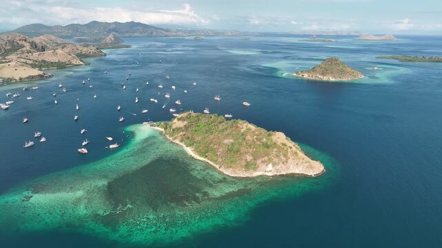 Aerial view of Pulau Kelor with turquoise waters and numerous boats anchored nearby in Komodo, East Nusa Tenggara, Indonesia.