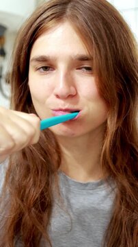Young woman brushing her teeth with a toothbrush in the morning. Close-up portrait of a smiling young woman brushing her teeth with a blue toothbrush during her morning hygiene routine