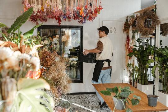 Young male florist carrying box in a colorful flower shop